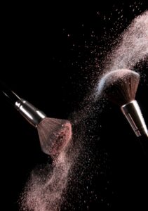 Pink powder cloud bursting from makeup brushes against a black background