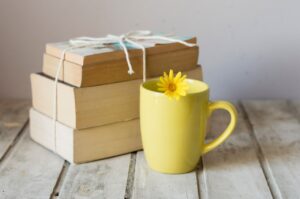 Stack of books tied with string next to a yellow mug with a small yellow flower on the rim, placed on a rustic wooden surface.