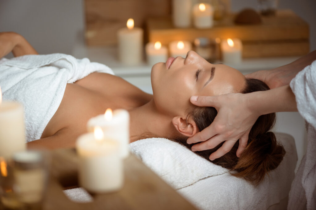 Young beautiful brunette girl having face massage relaxing in spa salon.